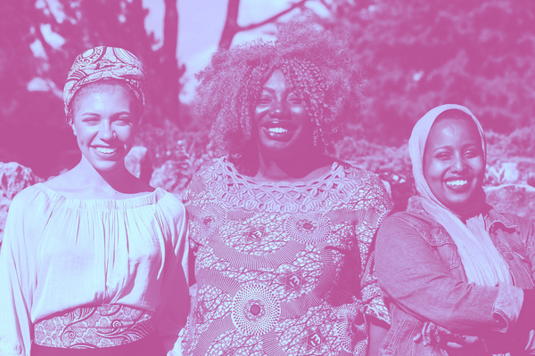 Three smiling Black immigrant women standing side by side.