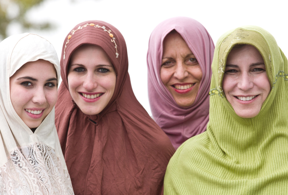 Photo of 3 women collaborating at a table. The woman at the focal point of the image is wearing a head scarf and writing on a piece of paper at the center of the 3 women.