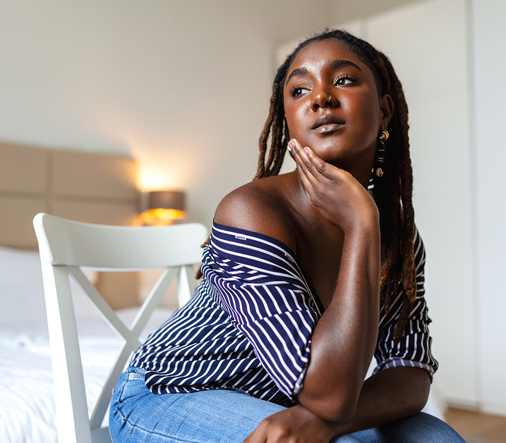 Young Black woman with chin in hand looking off to the side with a thoughtful but not sad expression.