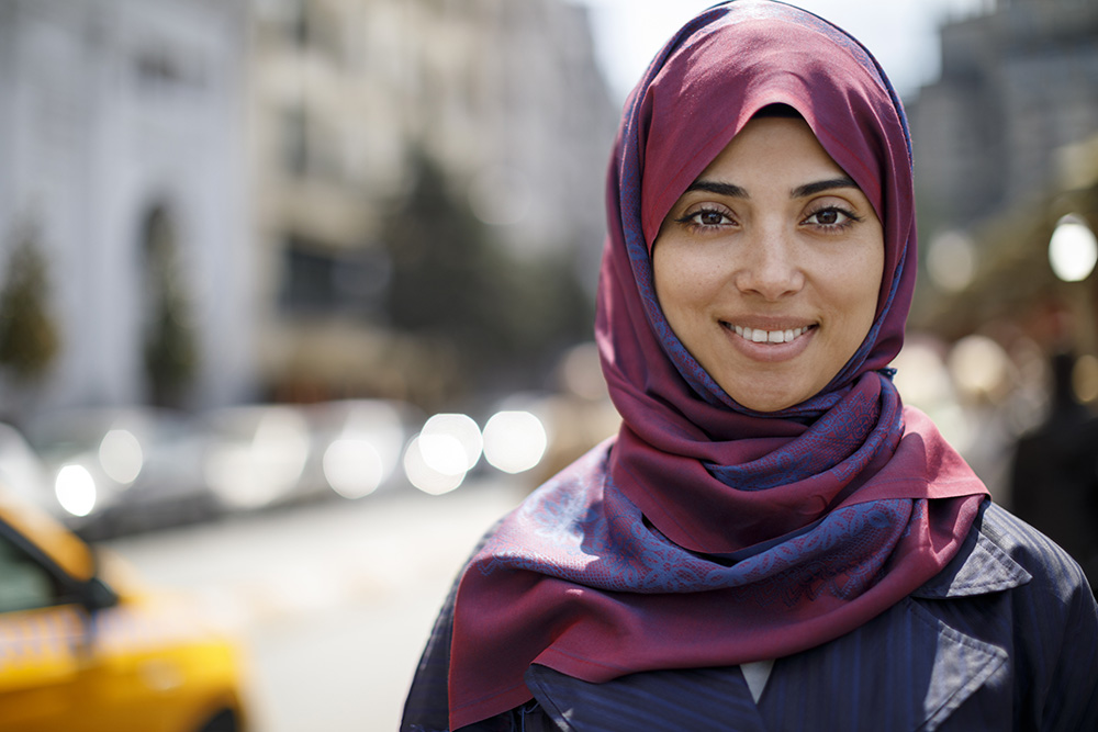 Woman in urban setting smiling and wearing head scarf