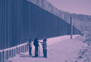 Immigrants stand next to a border fence at the U.S. Mexico border.