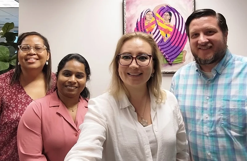 Three women and one men smiling in office hallway with artwork in background.