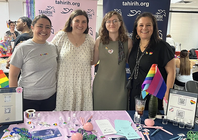 Four women stand in front of a table with Tahirih materials and rainbow LGBTQ+ supportive materials