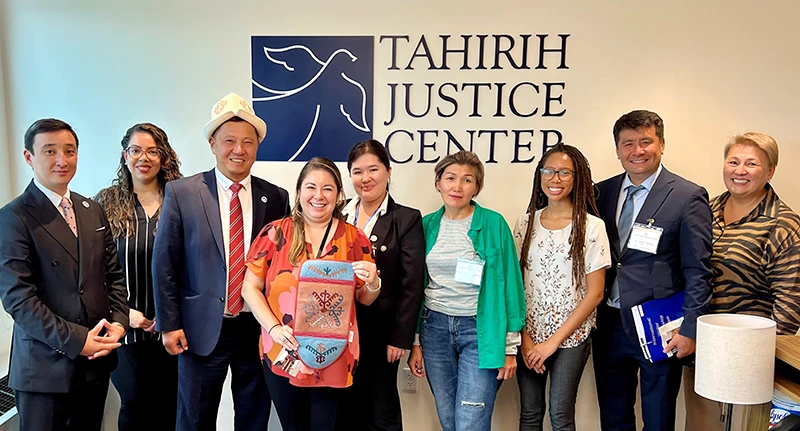 Row of smiling people in front of a Tahirih Justice Center wall logo