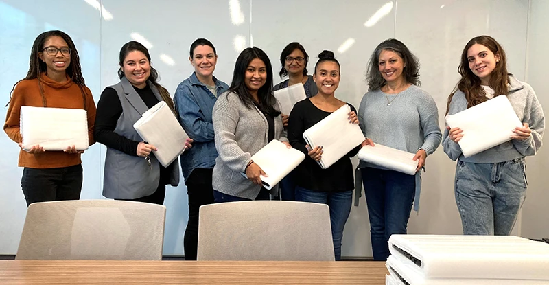 Eight women of different ethnicities smiling in a conference room holding laptops.