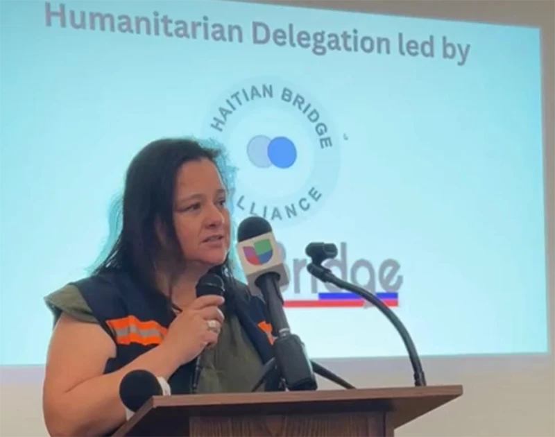 Woman speaks into microphone at podium in front of presentation screen.