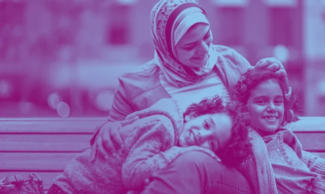 Woman with head scarf smiling down on two kids laughing with their heads on her lap
