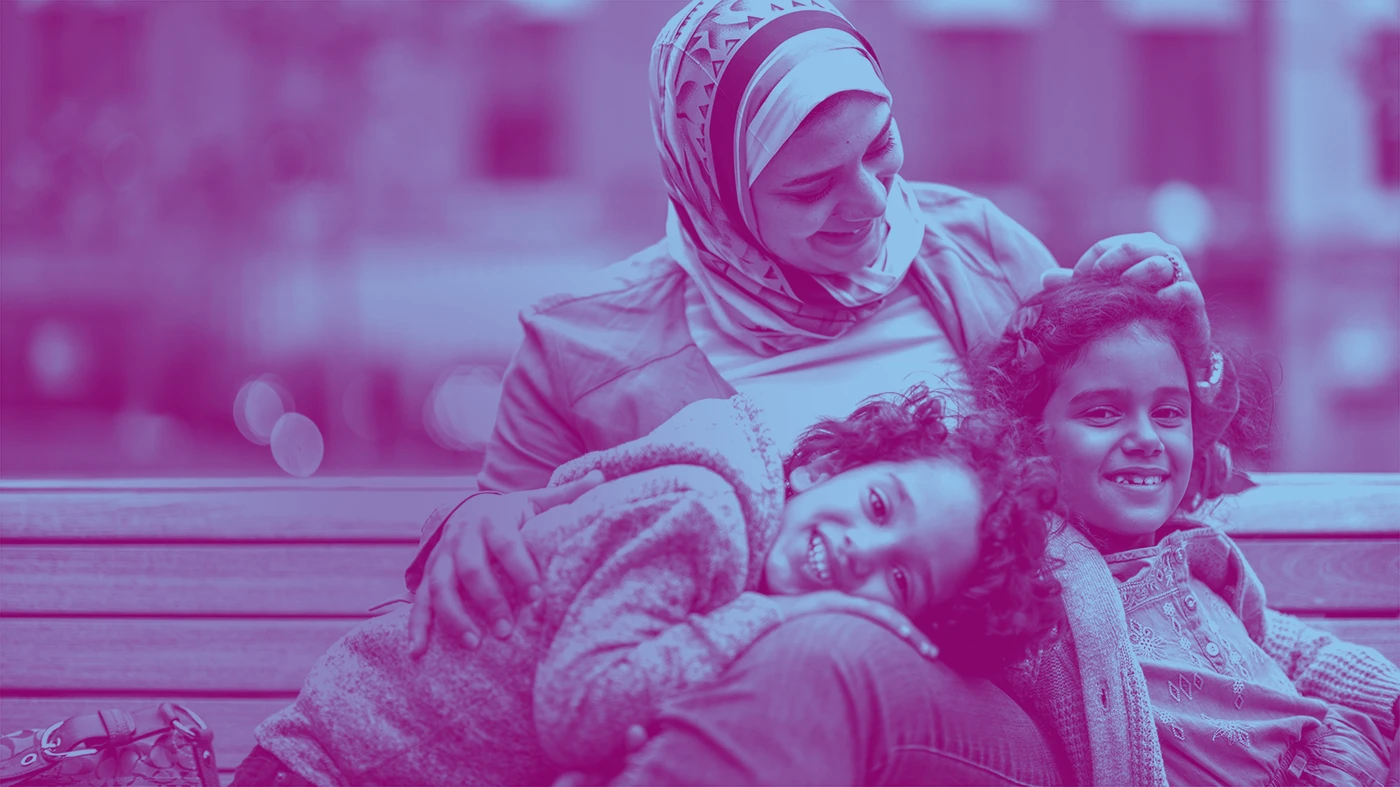 Woman with head scarf smiling down on two kids laughing with their heads on her lap