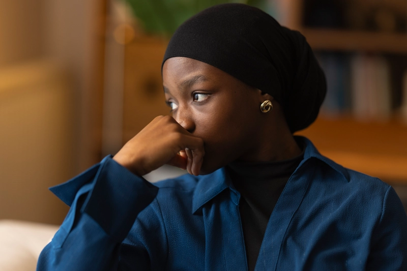 Young Black woman with head scarf looking aside with concerned expression.