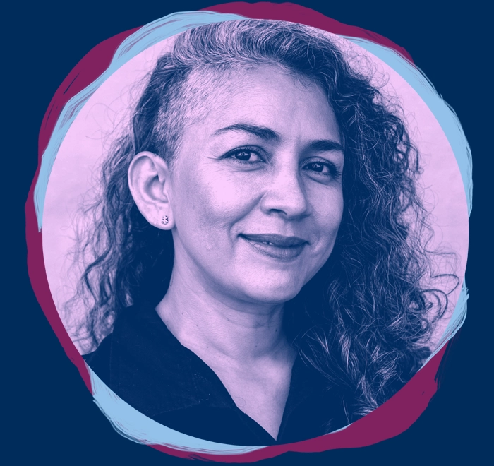 Middle aged woman with long curly hair and side shave on her head, with a confident, resilient expression and slight smile.